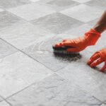 Hand of man wearing orange rubber gloves is used to convert scrub cleaning on the tile floor.