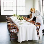 Waitress setting banquet table for dinner party in loft